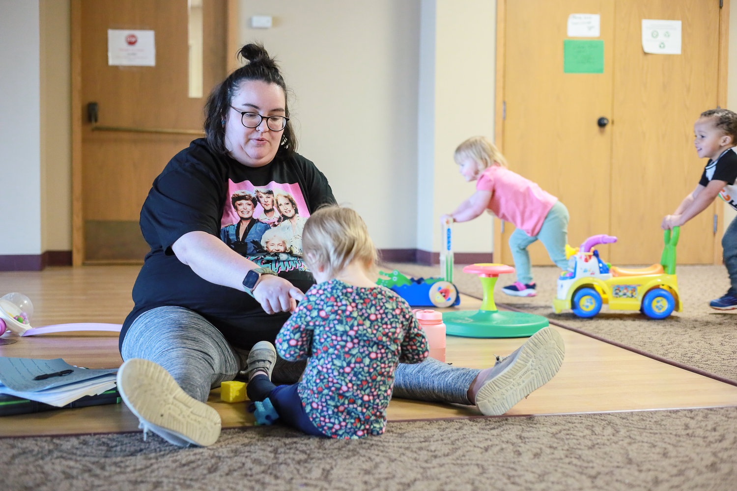 Amber Boone, lead teacher for 2-year-olds at Lighthouse Child and Family Development Center at Messiah Evangelical Lutheran Church, works with a child as others race push toys behind her.